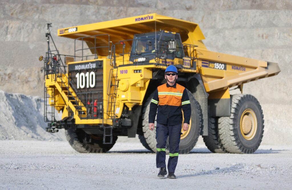 A worker in safety gear walking in front of a haul truck at an open-pit mine