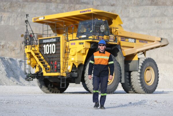 A worker in safety gear walking in front of a haul truck at an open-pit mine