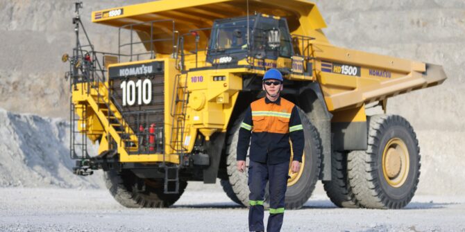 A worker in safety gear walking in front of a haul truck at an open-pit mine
