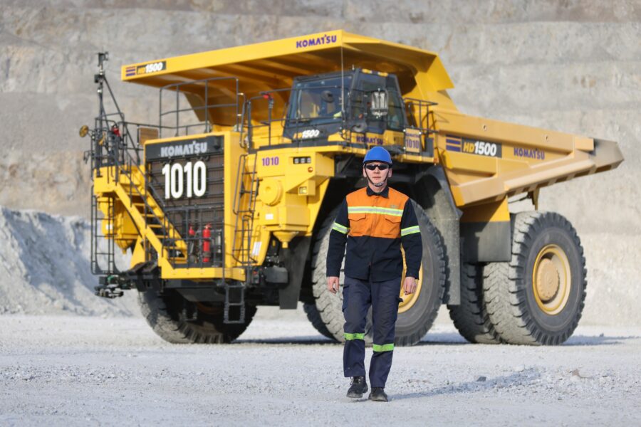 A worker in safety gear walking in front of a haul truck at an open-pit mine