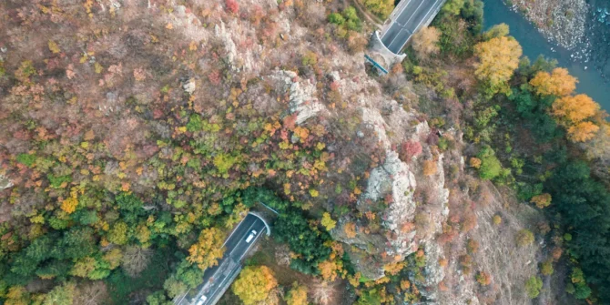 Drone aerial top down view of mountain road with tunnel, river and fall colour forest.
