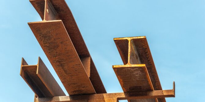 a photo looking up at metal structure beams, with the blue sky behind