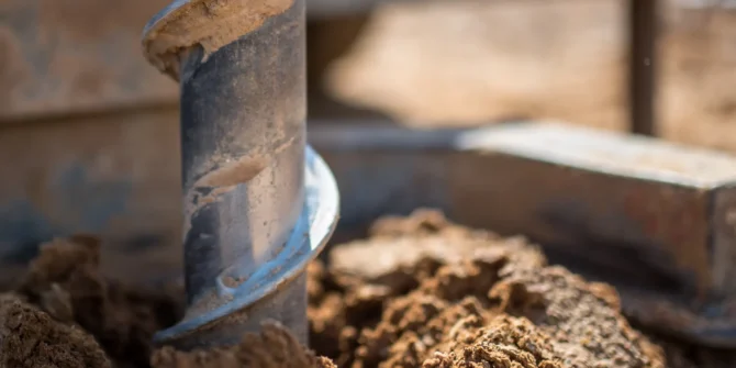 A close-up of a helical auger advancing during a geotechnical borehole, with soil cuttings being brought to the surface for visual logging and sampling as part of a site investigation. Shutterstock ID 1734495353