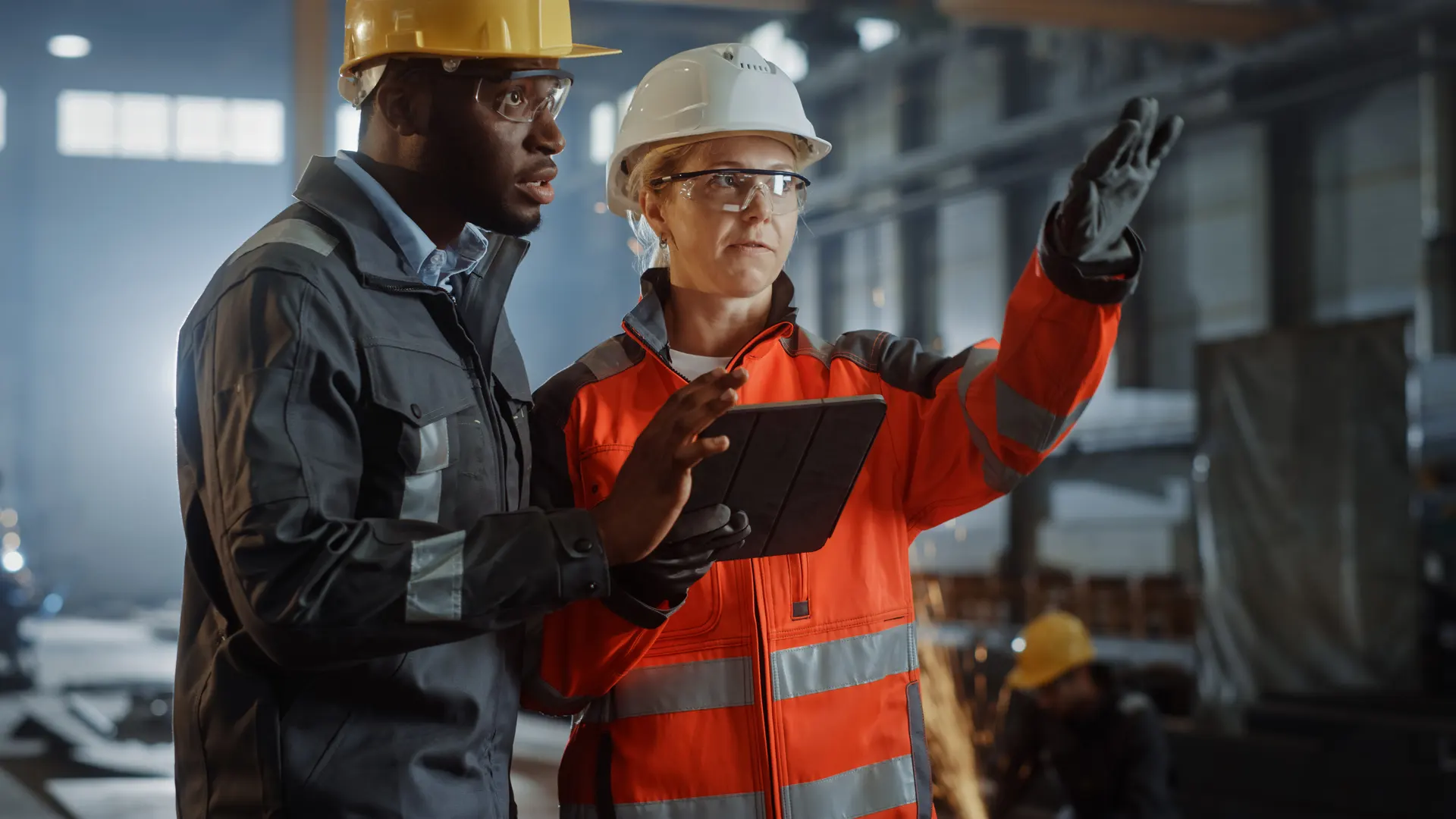 Two Heavy Industry Engineers Stand in Steel Metal Manufacturing Factory, Use Digital Tablet Computer and Have a Discussion. Black African American Industrial Specialist Talk to Female Technician. shutterstock_1870469560