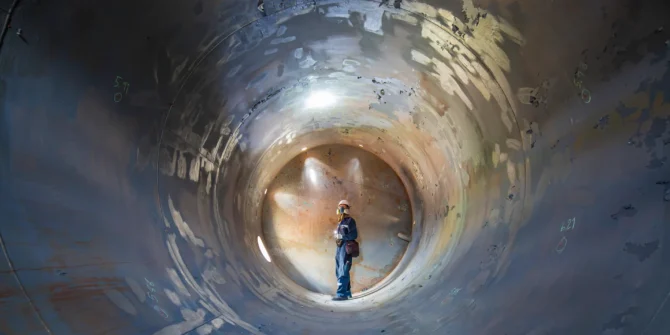 View down a tank tunnel of a person inspecting weld in underground tank wearing full facemask. AdobeStock_450434511