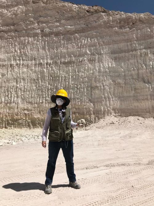 A photograph of Elisenda Rodriguez Perez at the special clay mines in Mexico, wearing outdoor gear, a mask, and a yellow hardhat.