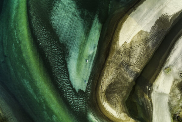Aerial view of texture featuring different shades of turquoise color and sand with two people kayaking. Location Waiwera, North Auckland, New Zealand.
