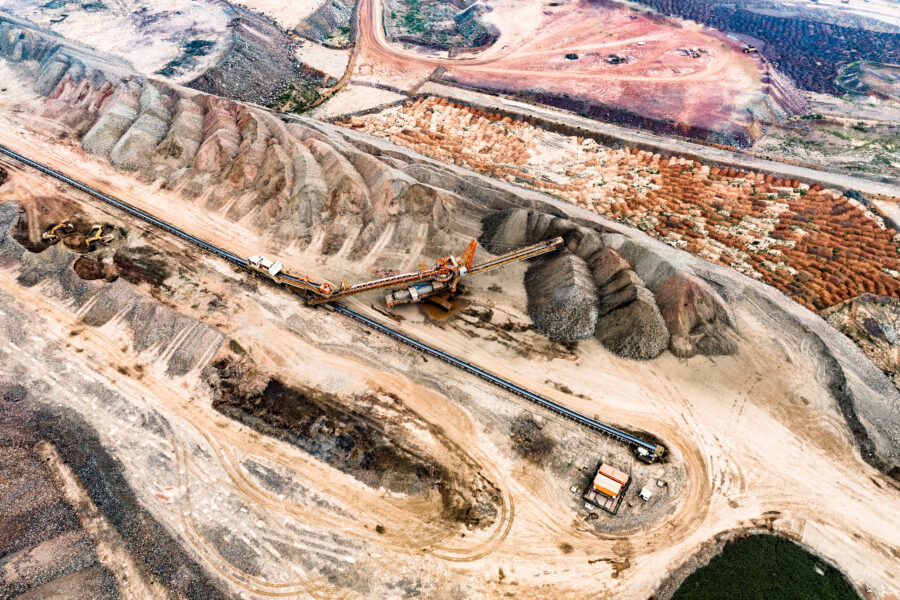 A large-scale open-pit mine featuring a long conveyor system, a stacker-reclaimer, and several excavators