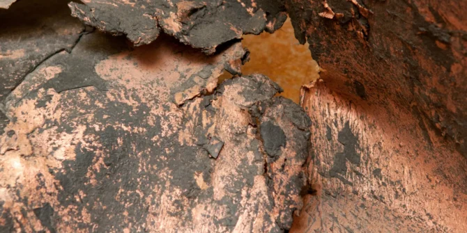 A close-up of copper rich rock, showing oxidised copper mineralisation with reddish-brown and dark grey tones along natural fractures. shutterstock_1871676403