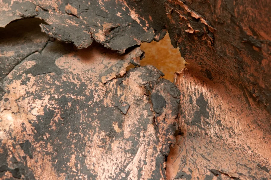 A close-up of copper rich rock, showing oxidised copper mineralisation with reddish-brown and dark grey tones along natural fractures. shutterstock_1871676403