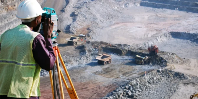 A surveyor at an open-pit copper mine in Zambia, peers through his survey instrument. This work records the daily changes in the open-pit, and help guide mining activities to the engineer's plans.
