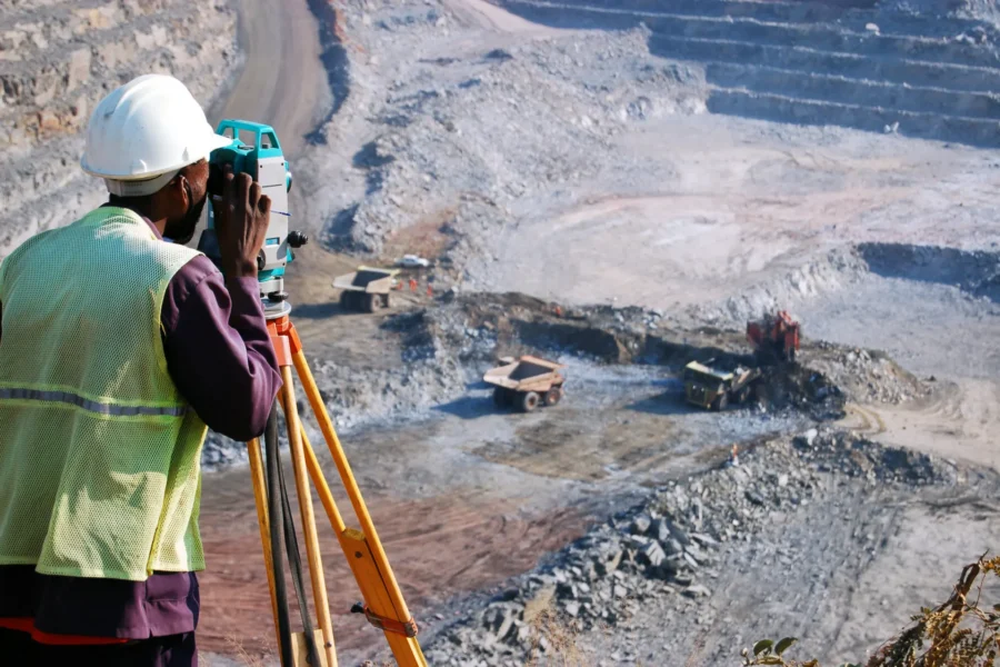 A surveyor at an open-pit copper mine in Zambia, peers through his survey instrument. This work records the daily changes in the open-pit, and help guide mining activities to the engineer's plans.
