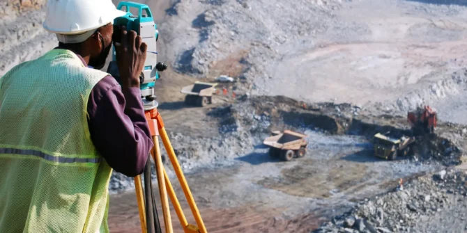 A surveyor at an open-pit copper mine in Zambia, peers through his survey instrument. This work records the daily changes in the open-pit, and help guide mining activities to the engineer's plans.