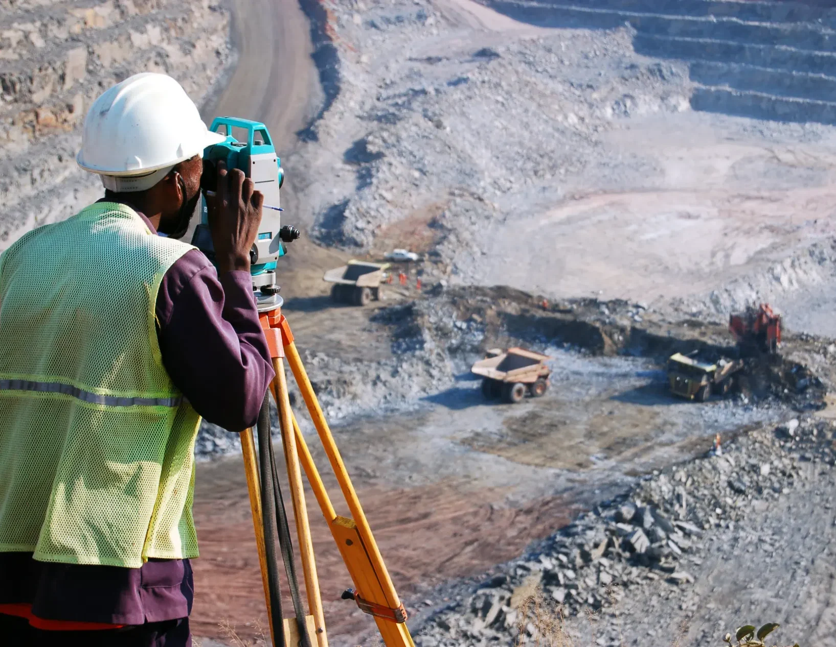 A surveyor at an open-pit copper mine in Zambia, peers through his survey instrument. This work records the daily changes in the open-pit, and help guide mining activities to the engineer's plans.