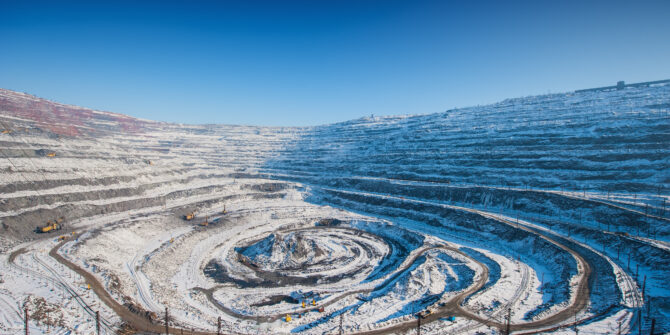 Wide view of a terraced open-pit mine covered in snow, with mining vehicles and railway tracks visible.