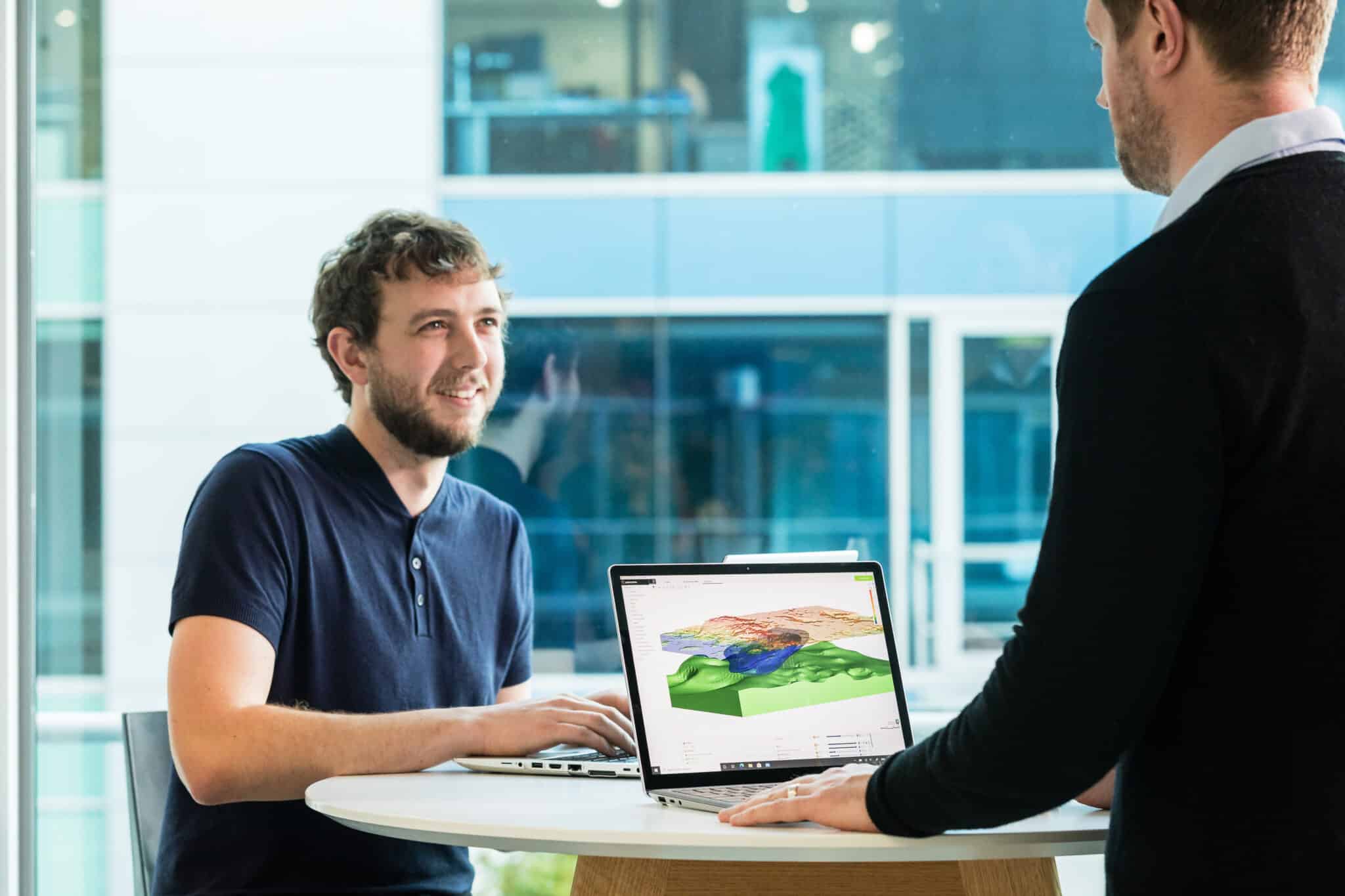 A photograph of 2 men at a table, with a 3D model in Seequent's Leapfrog Works visible on the laptop screen