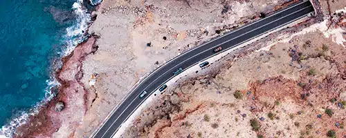 A picture of a a car coming out of an underground bridge continuing along a winding coastal road 