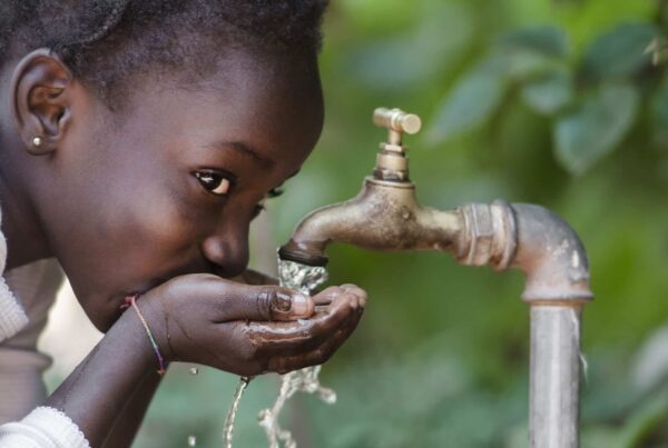 A young girl drinks from the palm of her hands from a running tap.
