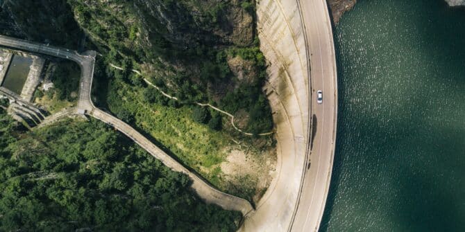 A photograph of a car driving on a winding road atop a dam wall