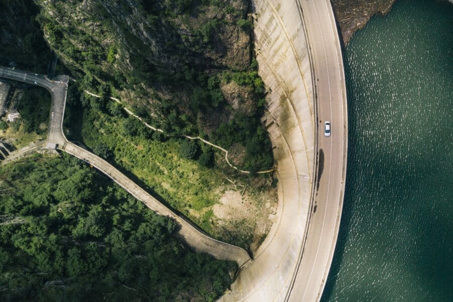 A photograph of a car driving on a winding road atop a dam wall