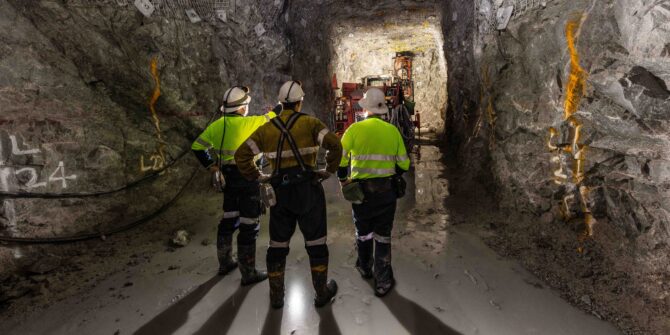 Miners in a tunnel inspecting a rock face.