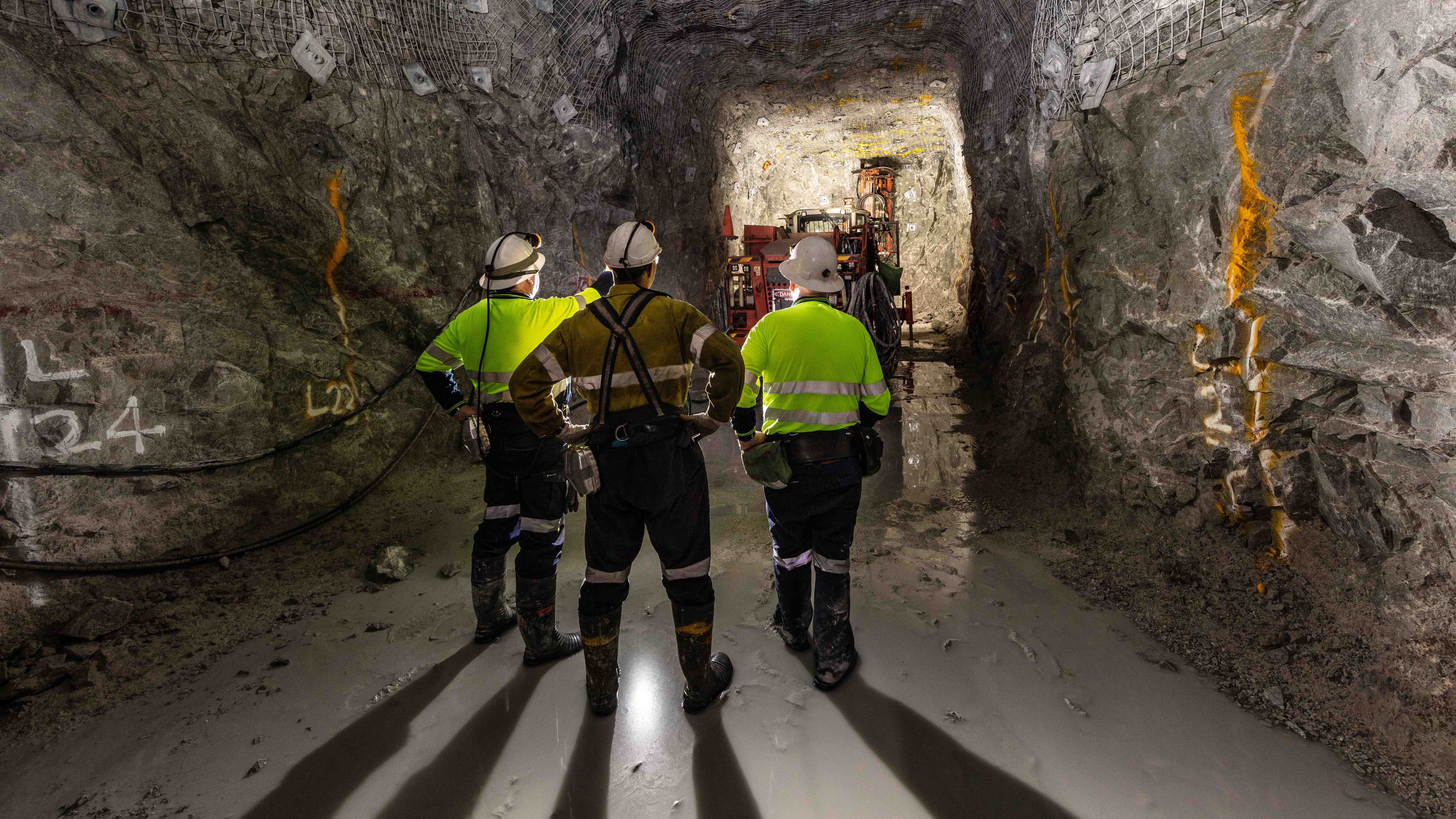 Miners in a tunnel inspecting a rock face.