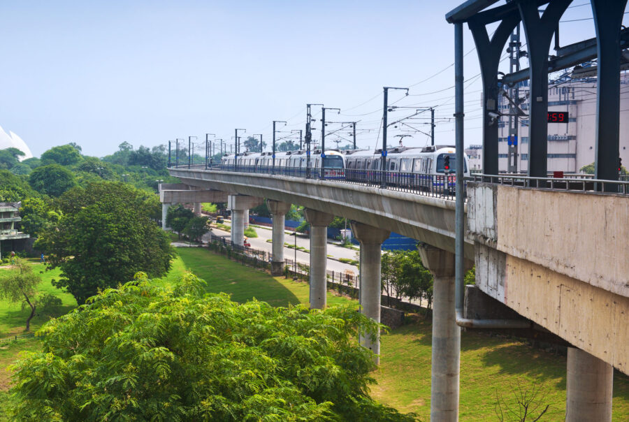 A rail bridge built across green space with Delhi's Lotus Temple in the background.