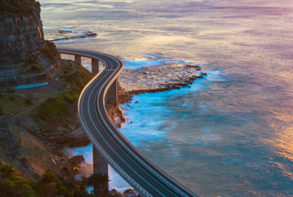 A photograph of a curved road on pillars along a mountainous coastline at sunset