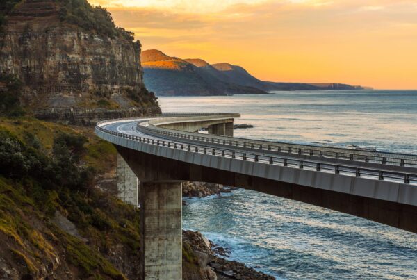 A photograph of a curved road on pillars along a mountainous coastline at sunset