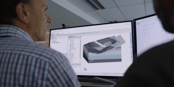 A photograph of 2 men looking at a 3D model from Seequent's GeoStudio on the screen