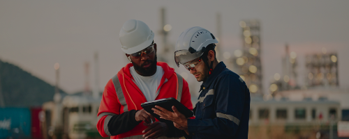 Two Engineers working to check safety quality control of oil and gas plant at sunset on a tablet. Oil and gas plant in background.